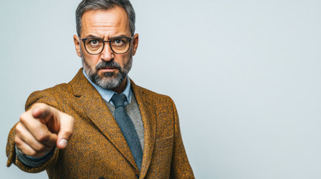 A man with glasses wearing a brown tweed suit points assertively in a plain background, conveying authority.の素材