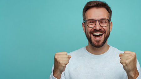Man with glasses smiles broadly and raises fists in excitement, expressing happiness and success.の素材