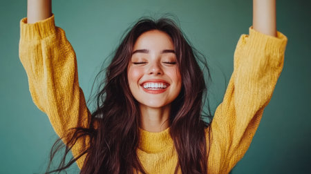 Young woman expresses happiness with a big smile and raised arms, wearing a cozy yellow sweater.の素材