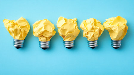 Crumpled yellow paper creates light bulbs, symbolizing creativity against a blue backdrop.の素材