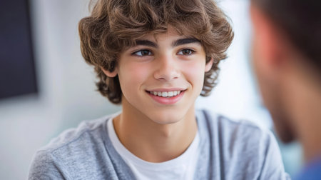 A cheerful young boy with curly hair smiles warmly while speaking with someone in a lively atmosphere.の素材