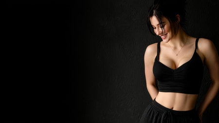 A woman smiles warmly while dressed in a black top and pants. She stands against a dark wall radiating positivity.の素材