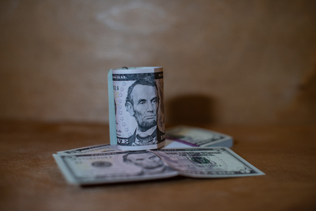 Five dollar bills in a roll lying on a bundle of banknotes.の写真素材