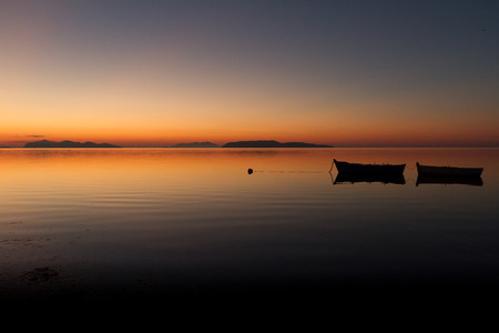 A warm sunset on a calm water, with Islands in the backgroundの写真素材