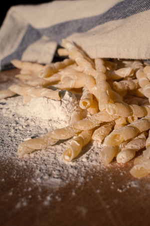 Homemade pasta lying on a wood cutting board, partially covered with a clothの写真素材