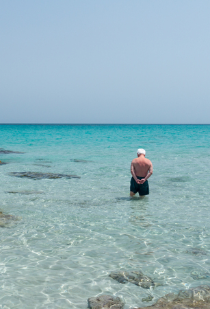 An old man is standing in the middle of the sea, probably evaluating if the temperature of the water is to cold to have a swim.の写真素材