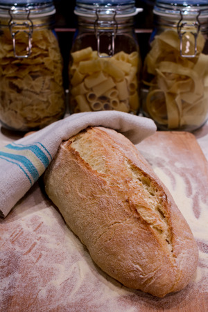A fresh-baked bread on a wood cutting board, with three pasta bowls in the background, representing concepts as Italian food, Homemade food, Warmth, Tradition, etc...の写真素材