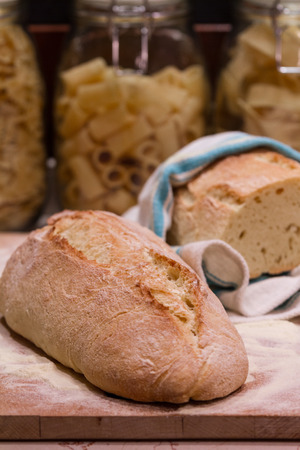 A fresh-baked bread on a wood cutting board, with three pasta bowls in the background, representing concepts as Italian food, Homemade food, Warmth, Tradition, etc...の写真素材