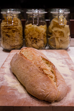 A fresh-baked bread on a wood cutting board, with three pasta bowls in the background, representing concepts as Italian food, Homemade food, Warmth, Tradition, etc...の写真素材