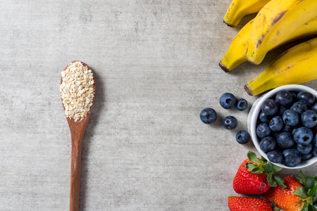 Background with a spoon full of oats and some fresh healthy fruits on a wooden table. Bananas, Blueberries and strawberries. top view. Copy space.の写真素材