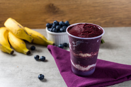 Brazilian frozen aÃ§ai berry ice cream on a plastic cup with oatmeal flakes layers. strawberries and blueberries on background. Summer menu front view.の写真素材