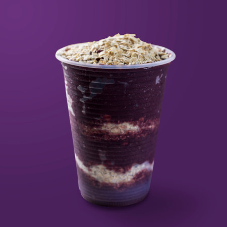 Brazilian frozen aÃ§ai berry ice cream on a plastic cup with oatmeal flakes. isolated on purple background. Summer menu front view.の写真素材