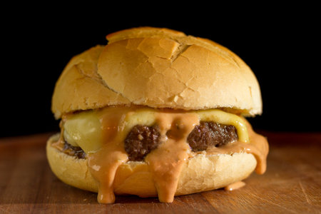 Close up of a homemade classic burger on a chopping wood board, on black background.の写真素材