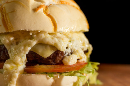 Close up of a homemade burger with extra cheese on a chopping wood board, on black background.の写真素材
