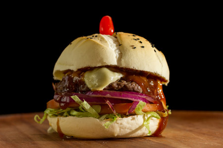 Close up of a homemade burger with salad and barbecua sauce on a chopping wood board, on black background.の写真素材