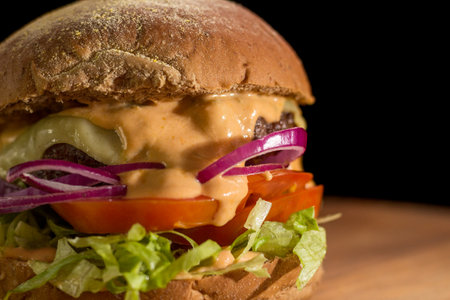 Close up of a homemade burger with salad on a chopping wood board, on black background. Australian bread.の写真素材