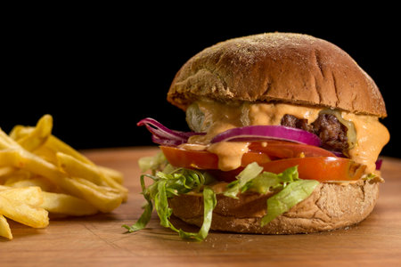 Close up of a homemade burger with salad on a chopping wood board, on black background. Australian bread.の写真素材