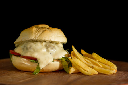 Close up of a homemade burger with extra cheese on a chopping wood board, on black backgroundの写真素材