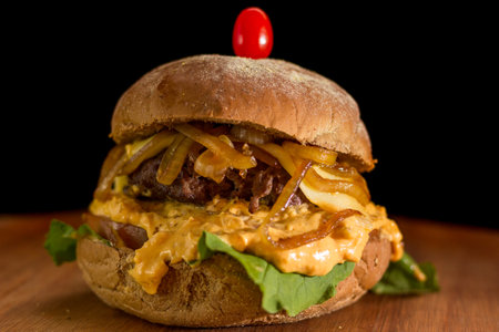 Close up of a homemade burger with onions and cheddar on a chopping wood board, on black background.の写真素材