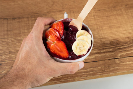 Hand holding an Brazilian AÃ§ai Bowl with Banana and Strawberry on a wooden background.の写真素材
