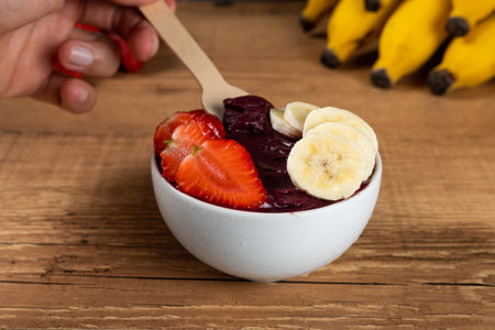 Hand holding an Brazilian AÃ§ai Bowl with Banana and Strawberry on a wooden background.の写真素材