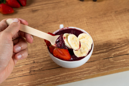 Hand holding an Brazilian AÃ§ai Bowl with Banana and Strawberry on a wooden background.の写真素材