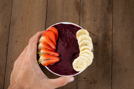 Man holding White Bowl of Brazilian Frozen AÃ§ai Berry with Banana and Strawberry. on a wooden desk.の写真素材