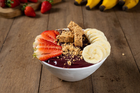 White Bowl of Brazilian Frozen AÃ§ai Berry With PaÃ§oca, Strawberry and Banana. on a wooden desk and fruits on background.の写真素材