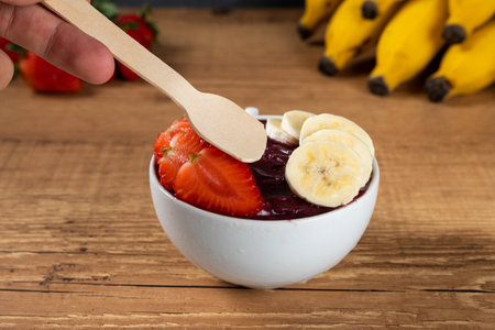 Hand holding an Brazilian AÃ§ai Bowl with Banana and Strawberry on a wooden background.の写真素材