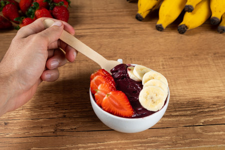 Hand holding an Brazilian AÃ§ai Bowl with Banana and Strawberry on a wooden background.の写真素材