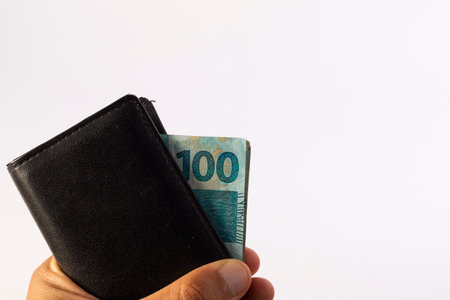 a man's hand holding a wallet with Brazilian 100 reais notes.の写真素材