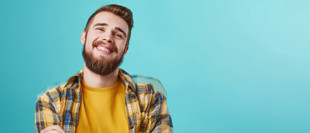 Portrait of a smiling young man with a beard in a yellow shirt on a blue backgroundの素材
