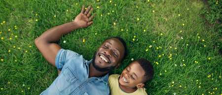 cheerful african american father and son lying on green grassの素材