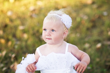 little girl in a white wedding dress is on the grassの写真素材
