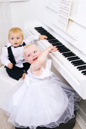 boy and girl playing in a concert dress on a white pianoの写真素材