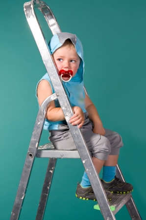 The boy sits on a ladder, in the hood, and with a pacifier on a green backgroundの写真素材