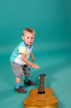 The boy reaches for the guitar, on a green backgroundの写真素材