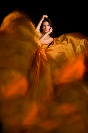 beautiful girl in the orange dress from flying fabric on a black backgroundの写真素材
