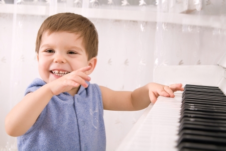 Laughing boy plays on a white piano in a bright roomの写真素材
