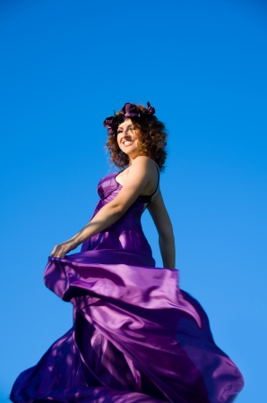 portrait of a beautiful girl with curly hair flying in the purple dress on the background of skyの写真素材