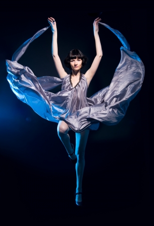girl in a gray dress flying on a black background with blue backlightの写真素材