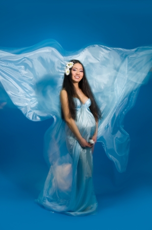 Asian pregnant woman in a silk dress on a blue background. Shooting with a mixed lightの写真素材