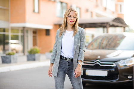 laughing beautiful blonde girl in a jacket, with red lipstick, against the backdrop of a car