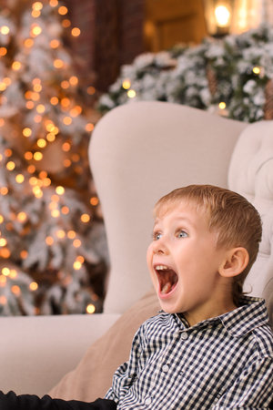 happy little blond boy next to his mother lying on the floor, shows an open palm, against the background of a christmas treeの写真素材