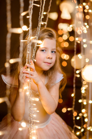 happy girl sits in a red toy wooden car, looks out of the window, among white decorative snowの写真素材