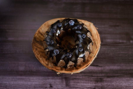 chocolate cupcake decorated with blueberries with icing on a wooden birch stand, on a dark...