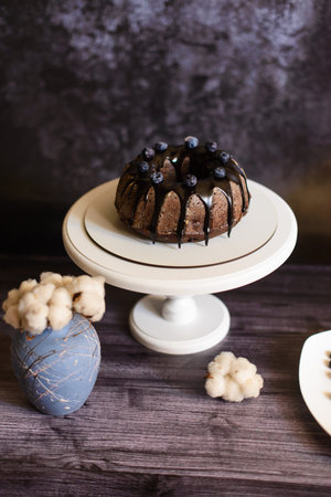 chocolate cupcake with icing on a white plate and a stand with a vase with a cotton flower, on a dark backgroundの写真素材