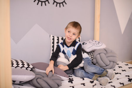 A boy in casual clothes, a vest and jeans, sits in a bed in a children's roomの写真素材
