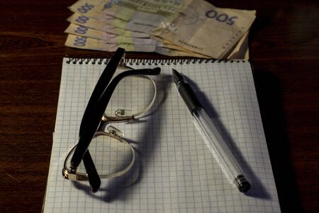 Notebook glasses pens and money on the table.の写真素材