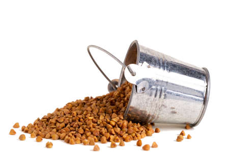 Scattered buckwheat and a metal bucket close-up on a white background. Isolate.の写真素材